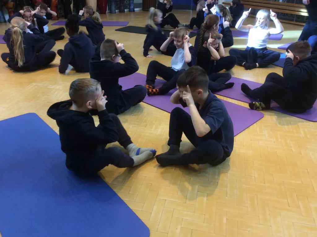 Children learning partner yoga and coordination techniques in a school wellbeing session near Manchester